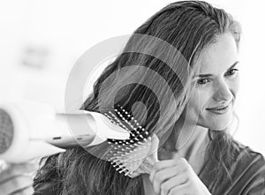 Woman brushing and blow drying hair in bathroom