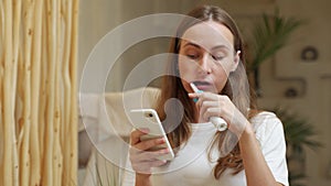 Woman brushing teeth and reading message on phone from bathroom. Girl with smartphone using toothbrush, checking social