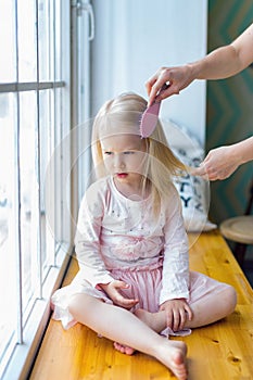 Woman brushing young girl`s hair while sitting near window