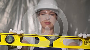 Woman builder in blue overalls and white hard hat helmet with level.