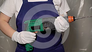 Woman builder in blue overalls and white hard hat helmet with puncher.