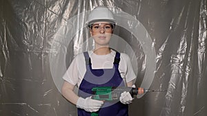 Woman builder in blue overalls and white hard hat helmet with puncher.