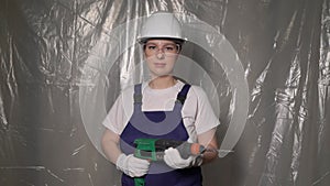 Woman builder in blue overalls and white hard hat helmet with puncher.