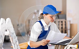 Woman builder checking documentation, using laptop