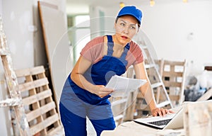 Woman builder checking documentation, using laptop