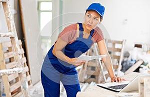 Woman builder checking documentation, using laptop