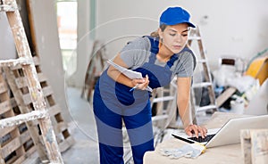 Woman builder checking documentation, using laptop