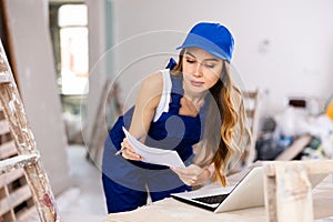 Woman builder checking documentation, using laptop
