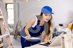 Woman builder checking documentation, using laptop