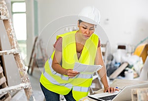 Woman builder checking project documentation and using laptop