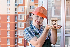 Woman in builder helmet holding house model and keys