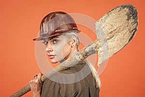 woman builder in protective helmet and boilersuit hold shovel on orange background, building