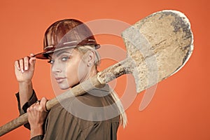 woman builder in protective helmet and boilersuit hold shovel on orange background, building