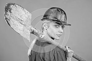 woman builder in protective helmet and boilersuit hold shovel on orange background, building