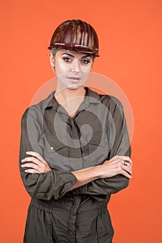 woman builder in protective helmet and boilersuit on orange background, engineering