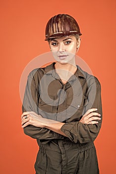 woman builder in protective helmet and boilersuit on orange background, engineering