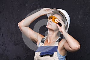Woman builder worker in uniform with white helmet and protective construction glasses on black background. Woman in workwear