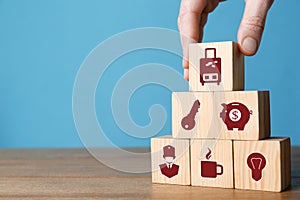 Woman building pyramid of cubes with different icons on wooden table against light blue background, closeup. Insurance concept