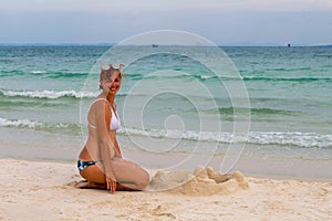 Woman building sand castle on beach. Relaxed smiling woman in bikini. Beach day activity.