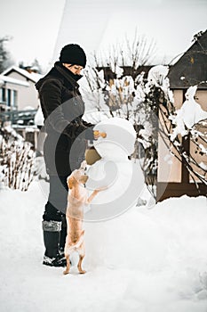 Woman building a snowman in the garden, jolly winter activity