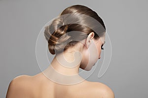 Woman with bun hairstyle on gray background. Bare back, shoulders and neck. Back view