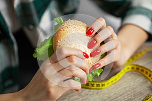 Woman with burger and measuring tape while dieting