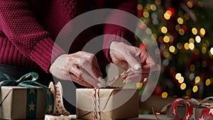 Woman in a burgundy sweater packs a lot of boxes with gifts in beautiful paper and ribbons, bows on the background of a Christmas