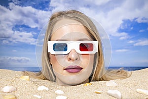 Woman buried in sand on beach with 3d glasses