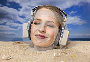Woman buried in sand on beach with headphones