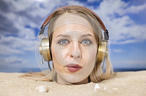 Woman buried in sand on beach with headphones