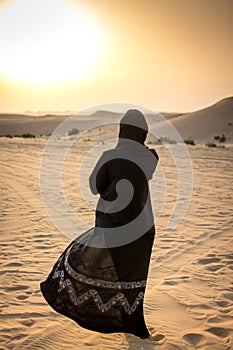 Woman in a burka Burqa walking over a middle eastern desert during sunset.