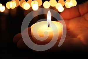 Woman with burning candle in darkness, closeup. Memory day