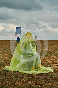 Woman in burqa on chair in field with white rose in her hands is reading book. concept