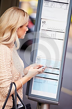 Woman At Bus Stop With Mobile Phone Reading Timetable