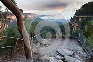 Woman at a bushwalking lookout with a view over a remote bushfire and smoke in the Blue Mountains, New South Wales, Australia.