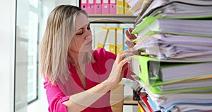 Woman business employee manually works with stacks of paper files to search and check unfinished archives