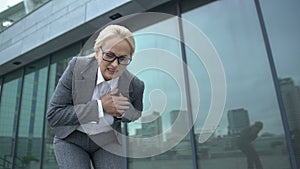 Woman in business suit throwing briefcase feeling strong pain in heart, dystonia