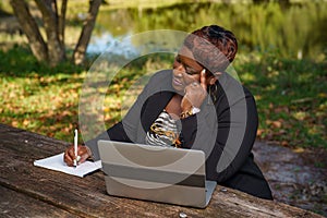 Woman in business teleworking in the park with laptop computer