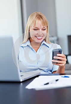 Woman busy on her cell phone. Happy young business woman reading text message with laptop on desk.