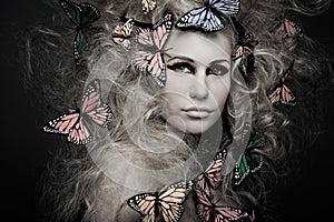 Woman with butterfly in big curly hair on black.