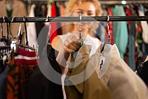 woman buyer choosing clothes in a store, blonde looks at a coat in a boutique on a hanger, selling things in a warehouse