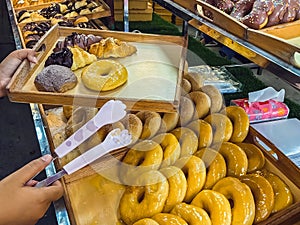 Woman buying donuts in baking store. Female choosing and buying fresh tasty pastry from shelves. Young woman choose freshly baked