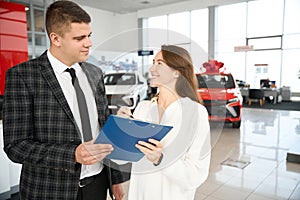 Woman buying new car signing contract standing with sales person in dealership