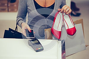 Woman buys shoes at the shop checkout, she is paying with contactless smartphone payment