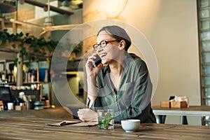 Woman at cafe making a phone call and using laptop computer. Beautiful young woman sitting at coffee shop working on laptop and