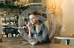 Woman at cafe making a phone call and using laptop computer. Beautiful young woman sitting at coffee shop working on laptop and