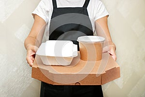 a woman cafe worker serves a completed takeaway order boxed pizza and a container with appetizers and soup in disposable
