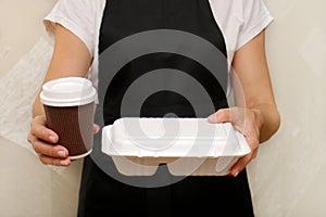 a woman cafe worker serves a completed takeaway order a glass of coffee and a container with food in disposable utensils