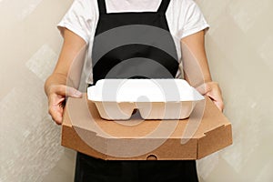 a woman cafe worker serves a completed takeaway order - pizza in a box and a container with food in disposable utensils