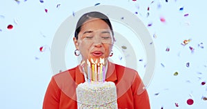 Woman, cake and blow candles in studio, confetti and birthday celebration with smile by blue background. Asian girl